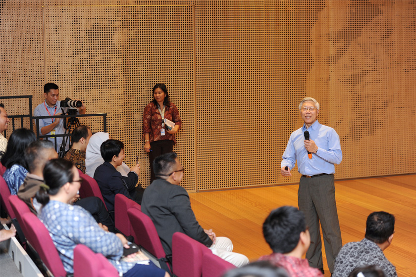 An older man with glasses and blue shirt is lecturing 